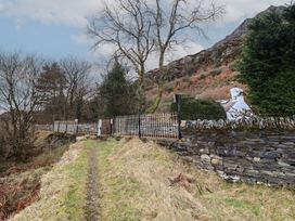 A grassy path leading to a metal gate with stone walls trees and a rural hillside in the background at Quarry Cottage in Blaenau Ffestiniog