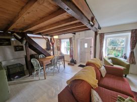 A living room with a red sofa green armchair wooden dining table and chairs under wooden ceiling beams at Quarry Cottage in Blaenau Ffestiniog