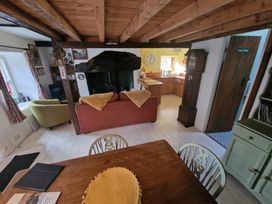 A living room with a red sofa yellow blankets a green armchair wooden beams and a kitchen area at Quarry Cottage in Blaenau Ffestiniog