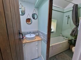 A bathroom with a wooden door round mirrors a sink and a bathtub with a shower at Quarry Cottage in Blaenau Ffestiniog