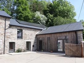 A stone and wood house exterior with solar panels on the roof and potted plants near the entrance at 3 Caddaford Barns in Buckfastleigh
