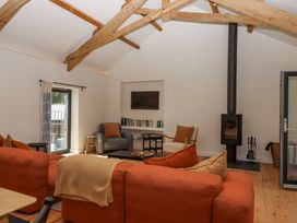 A living room with exposed wooden beams an orange sofa armchairs a wood stove and a bookshelf at 3 Caddaford Barns in Buckfastleigh