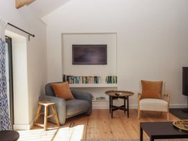 A sitting area with two armchairs a wooden stool a small round table and a built in bookshelf beneath a wall mounted television at 3 Caddaford Barns Buckfastleigh