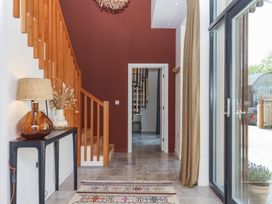 An entrance hallway with wooden staircase a console table with a lamp and vase a patterned rug and glass doors at 3 Caddaford Barns in Buckfastleigh