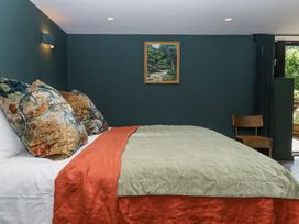 A bedroom with a bed covered with green and orange bedding and patterned pillows a chair and a painting on the wall at 3 Caddaford Barns in Buckfastleigh