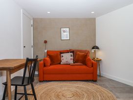 A small living area with an orange sofa and cushions a round woven rug a wooden table with a black chair and a framed picture on a patterned wall at 3 Caddaford Barns in Buckfastleigh