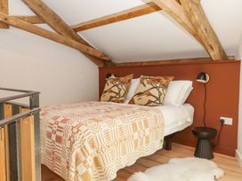 A small bedroom with exposed wooden beams a double bed with patterned pillows and blanket a black bedside lamp and stool and a white rug on wooden floor at 3 Caddaford Barns in Buckfastleigh