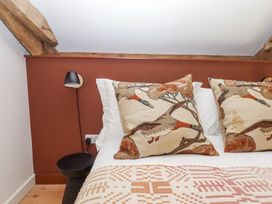 A bed with bird patterned pillows against a reddish wall with wooden beams and a black wall lamp at 3 Caddaford Barns in Buckfastleigh