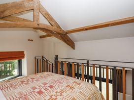 A bedroom loft area with a bed covered in a patterned quilt wooden beams on the ceiling and a railing overlooking a lower level at 3 Caddaford Barns in Buckfastleigh