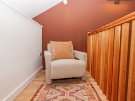 A small seating area with a beige armchair and cushion on a patterned rug next to a wooden railing at 3 Caddaford Barns in Buckfastleigh