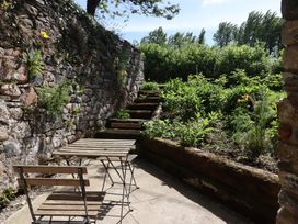An outdoor seating area with wooden chairs and a table next to stone walls and garden steps at 3 Caddaford Barns in Buckfastleigh