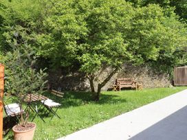 A garden area with a tree, wooden bench, table and chairs next to a stone wall at 3 Caddaford Barns in Buckfastleigh