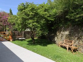A garden with a wooden bench and table set near a stone wall and a tree at 3 Caddaford Barns in Buckfastleigh