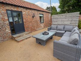 An outdoor patio area with a gray wicker sectional sofa a glass coffee table and a brick building at Partridge Place Burton Pidsea