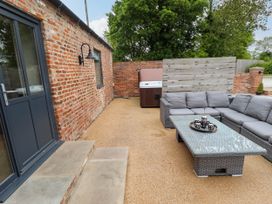 An outdoor patio with a gray wicker sectional sofa and glass coffee table near a brick wall and hot tub at Partridge Place in Burton Pidsea