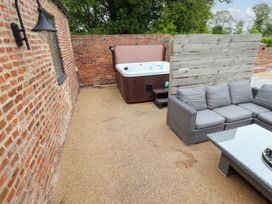 An outdoor patio with a hot tub a sectional sofa a glass coffee table and brick walls at Partridge Place in Burton Pidsea