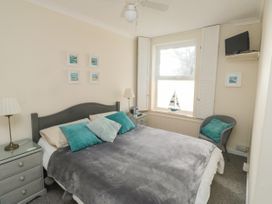 A bedroom with a double bed teal pillows bedside tables lamps a gray chair a window with a sailboat decoration and pictures on the wall at The White House in Torquay