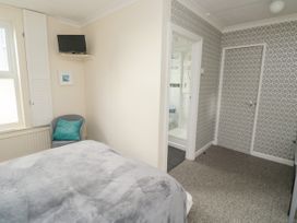 A bedroom with a bed covered in grey bedding a grey chair with a turquoise cushion a wall-mounted television a door leading to a bathroom and patterned wallpaper on one wall at The White House in Torquay
