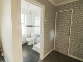 A bathroom with a toilet, shower, and a window next to a hallway with patterned wallpaper and a closed door at The White House in Torquay