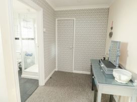 A hallway with a patterned wallpapered wall a door a small vanity table with a mirror and decorative items and an open door leading to a bathroom with a shower at The White House in Torquay
