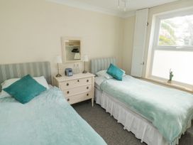A bedroom with two single beds with blue bedding a white chest of drawers with two lamps and bottles and a small statue on a windowsill at The White House in Torquay
