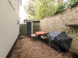 An outdoor patio area with a table covered by an orange cloth surrounded by four chairs and a covered barbecue grill next to a stone wall at The White House in Torquay