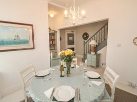 A dining area with a round table set for four with plates glasses and a flower vase a staircase and a small cabinet with a lamp in the background at The Link in Torquay