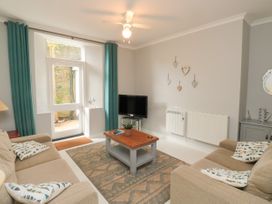 A living room with two beige sofas a wooden coffee table a television and teal curtains at The Link in Torquay