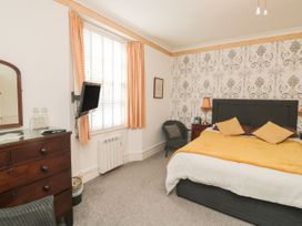 A bedroom with a bed pillows side table and lamp a window with curtains and a wall-mounted television at The Link in Torquay