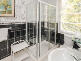 A bathroom with a glass-enclosed shower, white toilet, sink with glass shelf, towel rack, and window blinds at The Link in Torquay