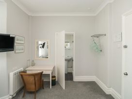 A room with a desk chair mirror and a wall-mounted television next to an open door leading to a bathroom at The Link in Torquay