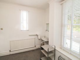 A small room with a sink a towel rail a radiator a metal shelving unit and windows with blinds at The Link in Torquay