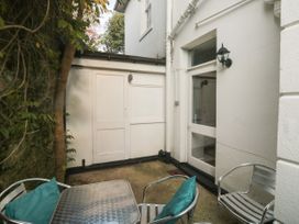 A small outdoor patio with metal table and chairs with teal cushions near white building and storage doors at The Link in Torquay