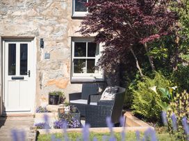 A stone house exterior with a door and window a black rattan chair with cushions and plants in a garden at Ynata in Trefor