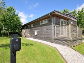 A wooden cabin with a deck and electric vehicle charger at 12 Meadow Retreat in Dobwalls