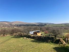 A rural landscape with a small wooden shed and greenhouse surrounded by grass and trees at Y Gweithdy Rhos Eirin in Maenclochog
