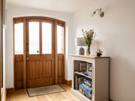 A hallway with a wooden door and a shelf displaying board games at Hoppers Barn Pancrasweek near Holsworthy