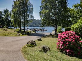 A pathway leading to a lake with a dock and flowering bushes at Treetops Beech Hill 13 ,Fallbarrow Park near Bowness-On-Windermere