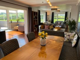 A dining table with a flower vase and cushioned chairs next to a living area with sofas and large windows at Ashlea in Launceston