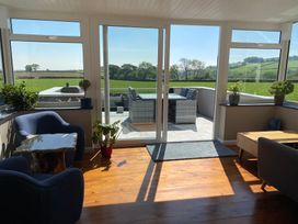 A sunlit living room with blue chairs plants and a wooden table overlooking a patio with outdoor furniture and green fields at Ashlea Launceston