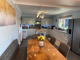 A kitchen with white cabinets a wooden dining table with chairs and a bench a vase with flowers a refrigerator and kitchen appliances at Ashlea in Launceston