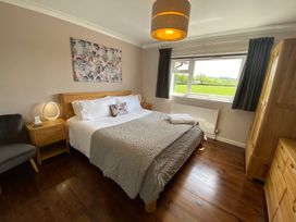 A bedroom with a double bed bedside tables a chair a wardrobe and a window showing a green field at Ashlea in Launceston