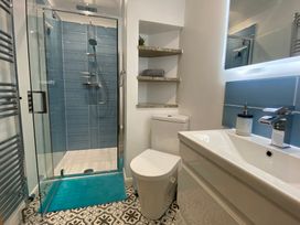 A bathroom with a glass shower, toilet, sink, shelves, and patterned floor tiles at Ashlea in Launceston