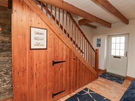 An entry hallway with a wooden staircase and under-stair storage a white door and blue rugs at Hares Form in Seahouses