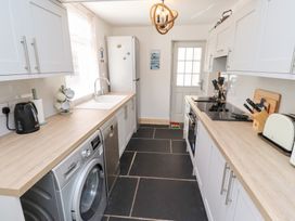A galley kitchen with white cabinets black appliances and a door at the end at Hares Form in Seahouses