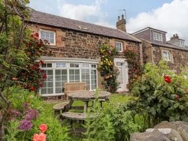 A garden with a stone cottage and a wooden table at Coble Cottage Craster