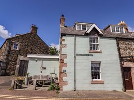 A house with a bench and sign on Dunstanburgh Road at Marie's Cottage in Craster