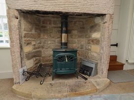 A living room with a wood stove in a stone fireplace at Marie's Cottage in Craster