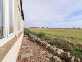 A side view of a house with a stone wall and grass at Beach View in Seahouses
