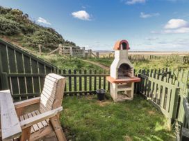 An outdoor area with a barbecue grill and wooden chair at Heather Cottages - Godwit, Bamburgh